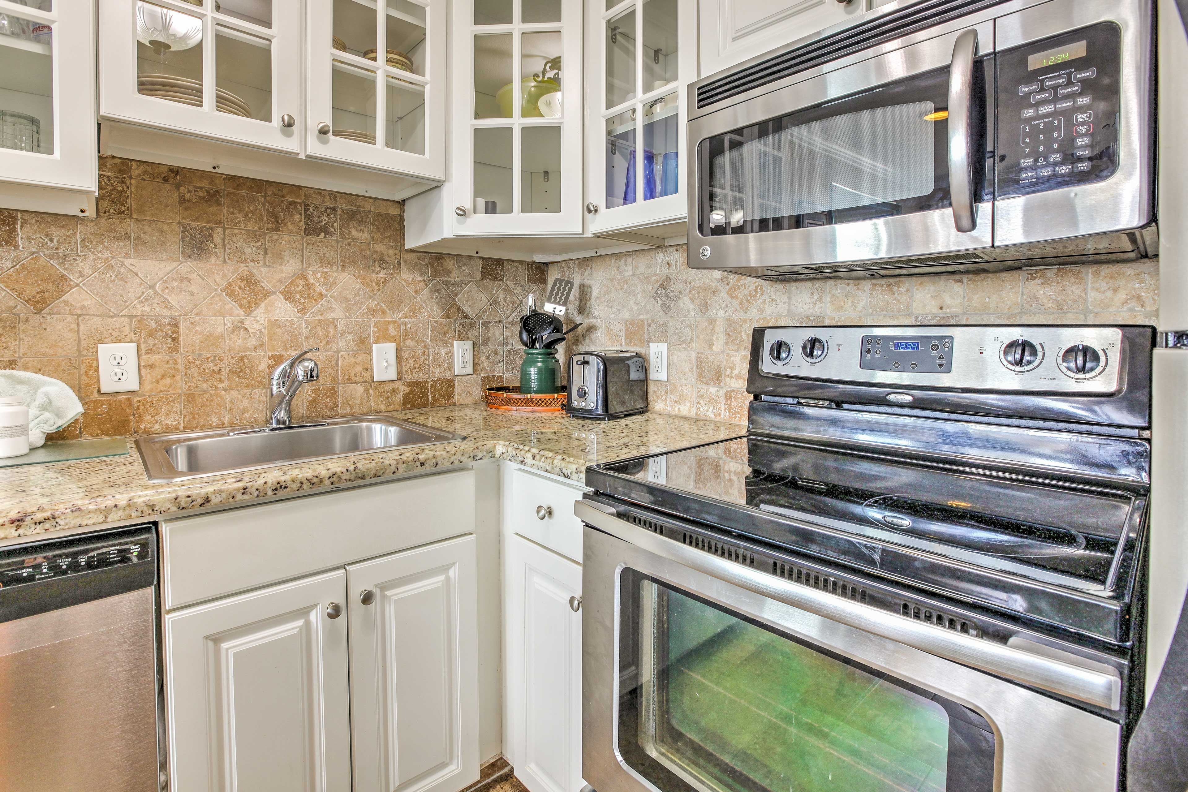 The kitchen features stainless steel appliances, granite countertops, and sleek, white cabinets.