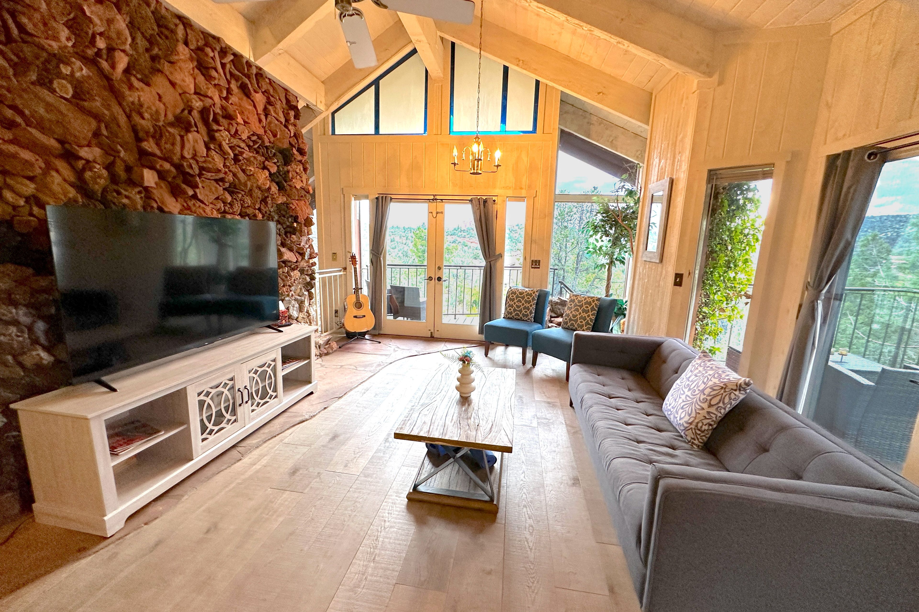 Living room w/ handcrafted stone wall, large bay windows, balcony w/ canyon view