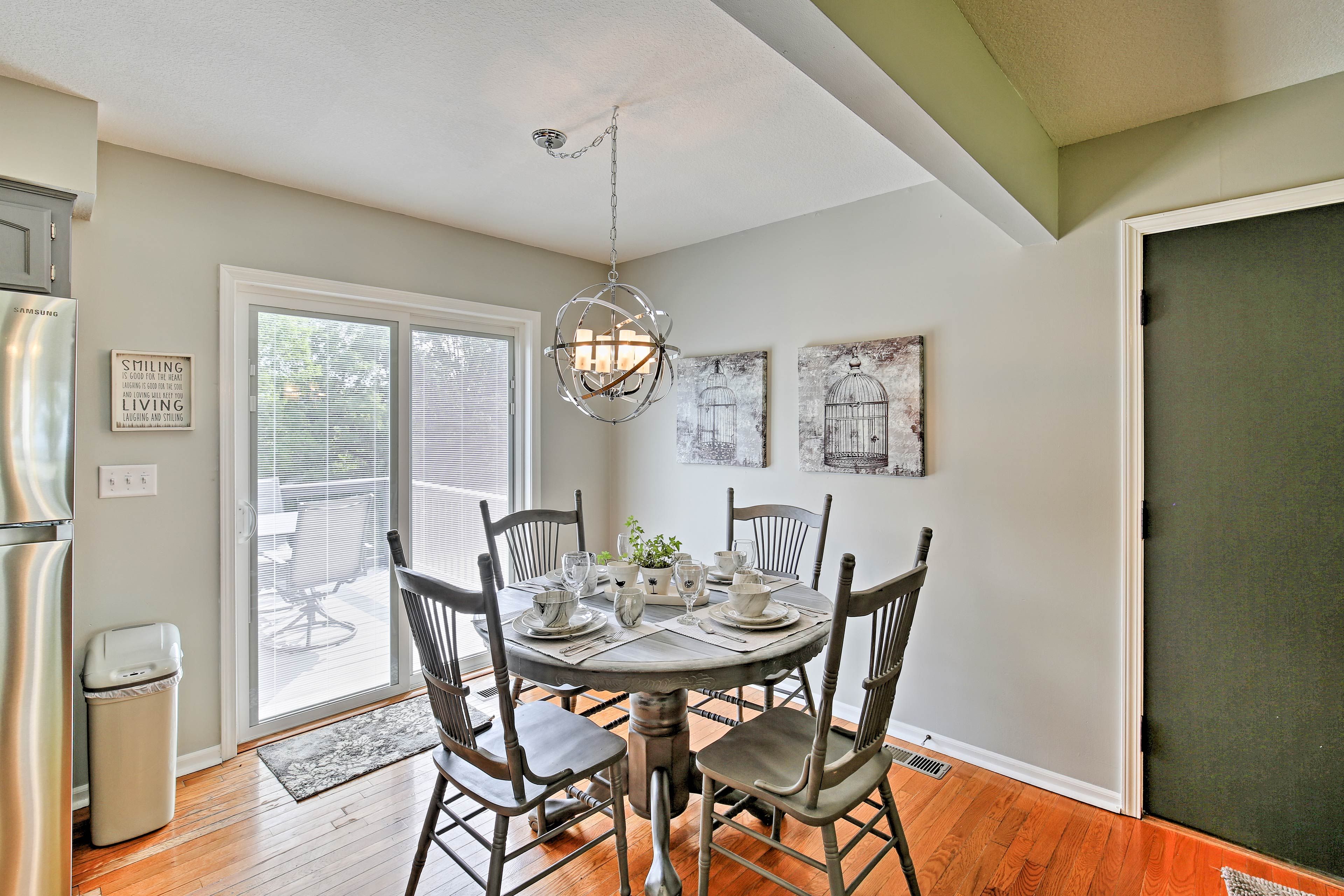 The adorable dining table is set for 4 under a modern chandelier.