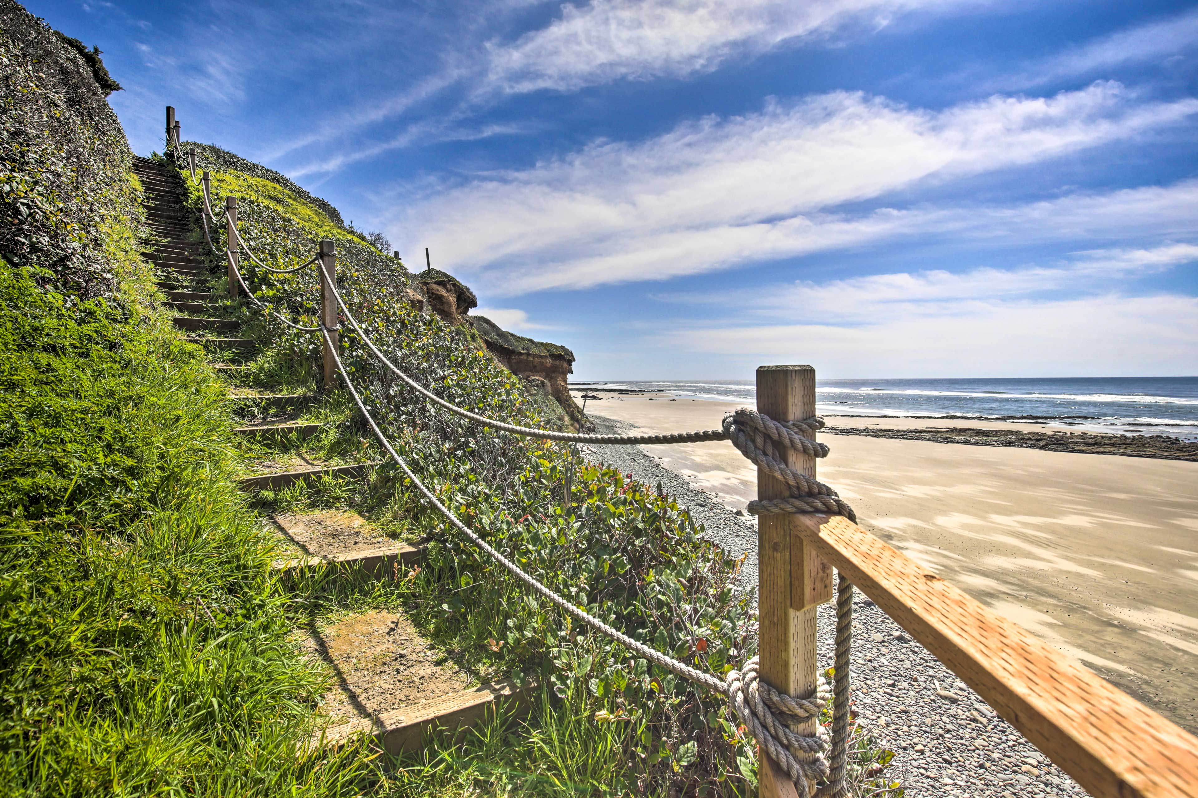 A steep cliff-side stairwell leads right to the sandy ocean shore.